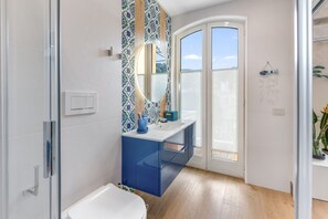 A bathroom with a white bathtub, a blue vanity, a large mirror, and a view through a glass door. - A Cozy Stay with Terrace in the Heart of Sorrento (Sorrento)