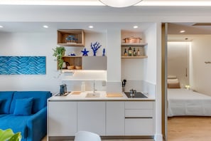 A modern kitchen with white cabinets, a blue sofa, and a bed in the adjacent room. - A Cozy Stay with Terrace in the Heart of Sorrento (Sorrento)