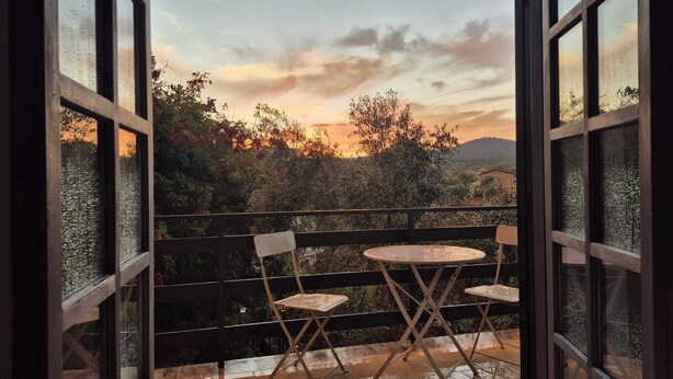 En åben balkon med udsigt til solnedgang, et bord og to stole.