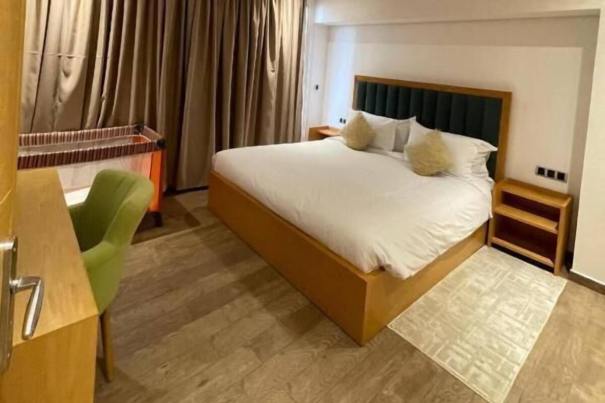 A bedroom with a large bed, a desk, a chair, and a wardrobe.