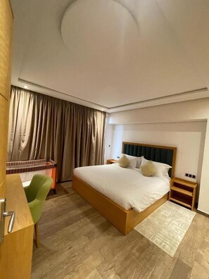 A bedroom with a large bed, a desk, a chair, and a wardrobe. - Hôtel Résidence Ramsis (Nador)