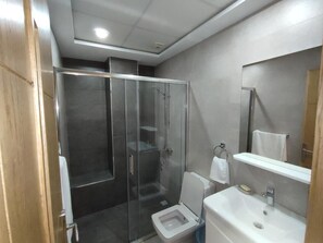 A modern bathroom with a glass shower enclosure, a toilet, and a sink with a mirror. - Hôtel Résidence Ramsis (Nador)