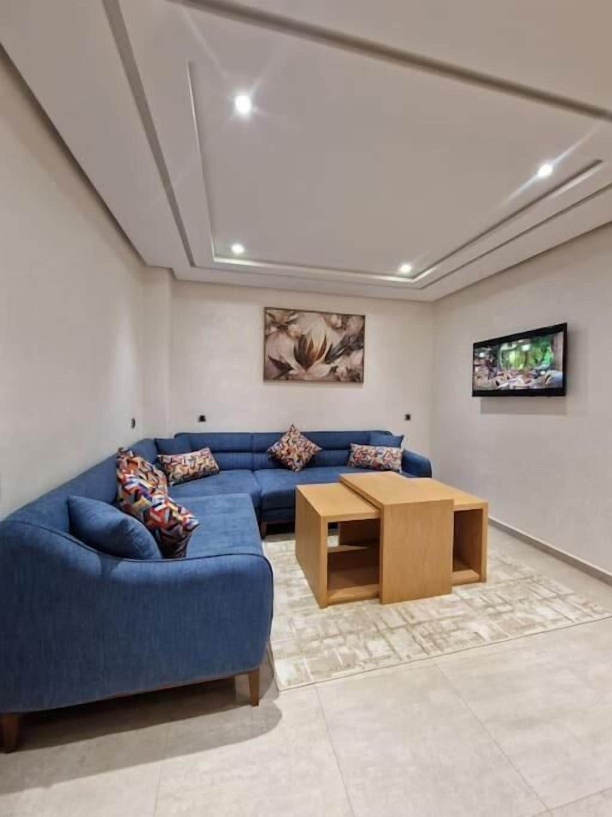 A modern living room with a blue sectional sofa, a wooden coffee table, and a flat-screen TV mounted on the wall.