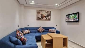 A modern living room with a blue sectional sofa, a wooden coffee table, and a flat-screen TV mounted on the wall.
