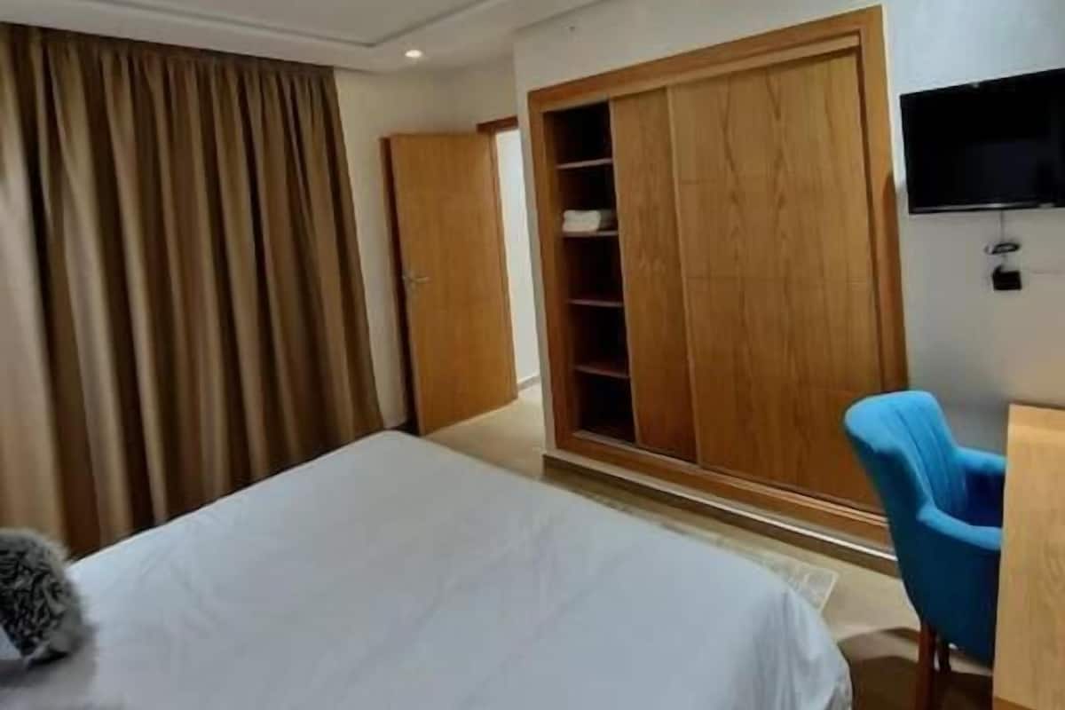 A hotel room with a bed, a wardrobe, a television, and a blue chair.