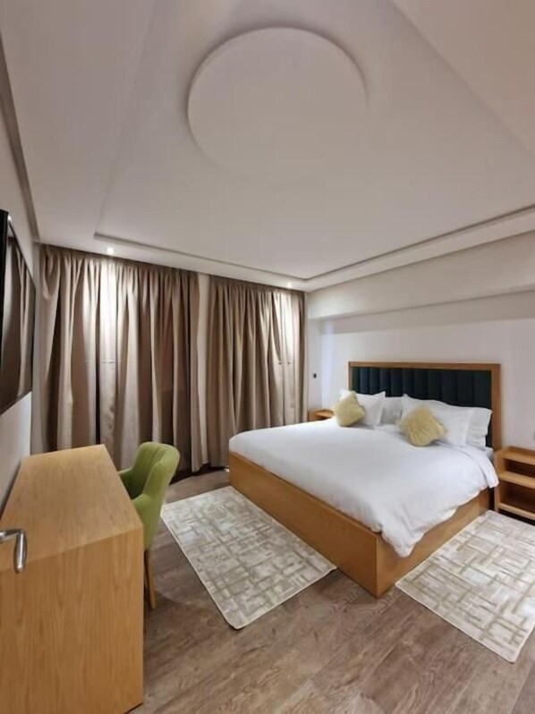 A modern hotel room with a large bed, a desk, a chair, and a view of the outdoors through the window. - Hôtel Résidence Ramsis (Nador)