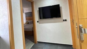 Ein Zimmer mit flachbildfernseher an der Wand, einem Holzschrank und einer Tür zu einem anderen Raum.