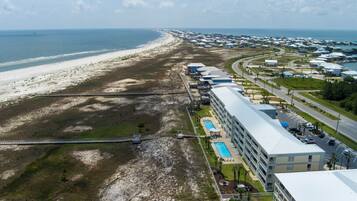 An aerial view of a coastal hotel with a long building adjacent to a beach, a swimming pool, and a parking area.