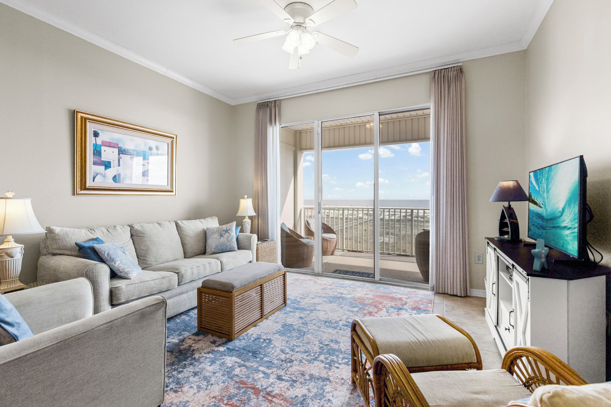 A hotel room with a balcony, a sofa, a TV, and a painting.