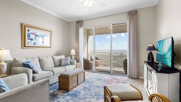 A hotel room with a balcony, a sofa, a TV, and a painting.