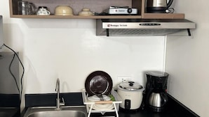 Eine kompakte Küche mit Spüle, Herd, Wasserkocher, Kaffeemaschine und Geschirrgestell.