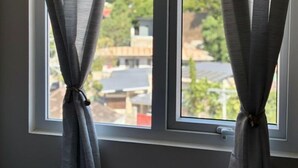 Ein Fenster mit zurückgebundenen Vorhängen, Blick auf eine grüne Landschaft mit Gebäuden.