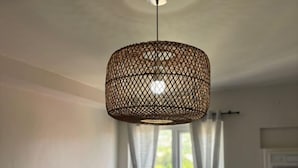 Ein Schlafzimmer mit Bett, Kopfstück, Fenster mit Vorhängen und einer Pendelleuchte.