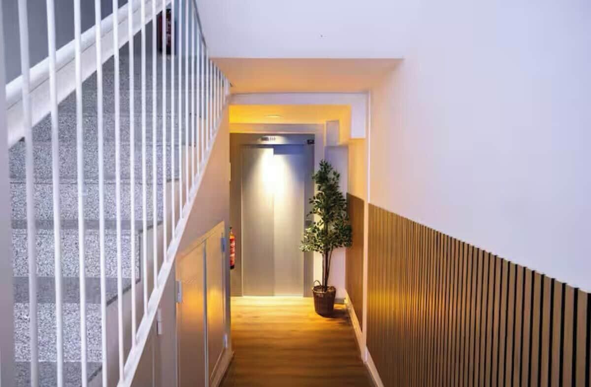 Un couloir d’hôtel moderne avec un plancher en bois, une rambarde blanche et une plante en pot.