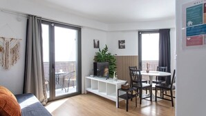 Un salon moderne comprenant un canapé, un téléviseur, une table à manger, des chaises et un balcon avec des rideaux.