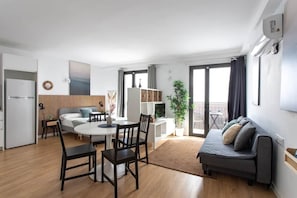 Een moderne woonkamer met een bank, eettafel, stoelen, een klein keukentje en een balkon met uitzicht.