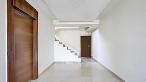 Un pasillo con una puerta de madera, una escalera y otra puerta al final.