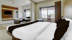 Una habitación de hotel moderna con una cama grande, un televisor de pantalla plana, un escritorio con una silla y una ventana con persianas.