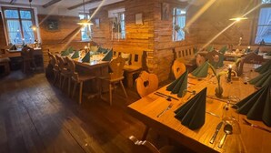 Tunnelmallinen ravintola, jossa on puupöydät ja -tuolit, kiviseinä ja riippuvalaisimet.