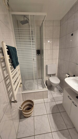 A bathroom with a glass shower enclosure, a toilet, a sink, and a towel rack. - Wildstein Vacation Rental—Mountain View (Bayrischzell)