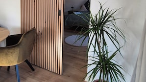 Huoneessa on liukuva puinen sermi, sänky, ruukkukasvi ja tuoli.