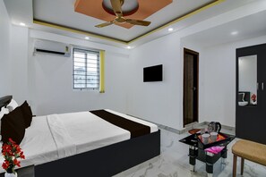 A modern hotel room with a bed, a desk, a chair, a ceiling fan, an air conditioning unit, a window, a flat-screen TV, and a door. - Classic With Balcony Mourigram Near Andul Road (Howrah)