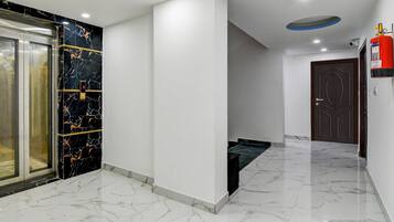 A hallway with a marble floor, a fire extinguisher, a door, and an elevator.