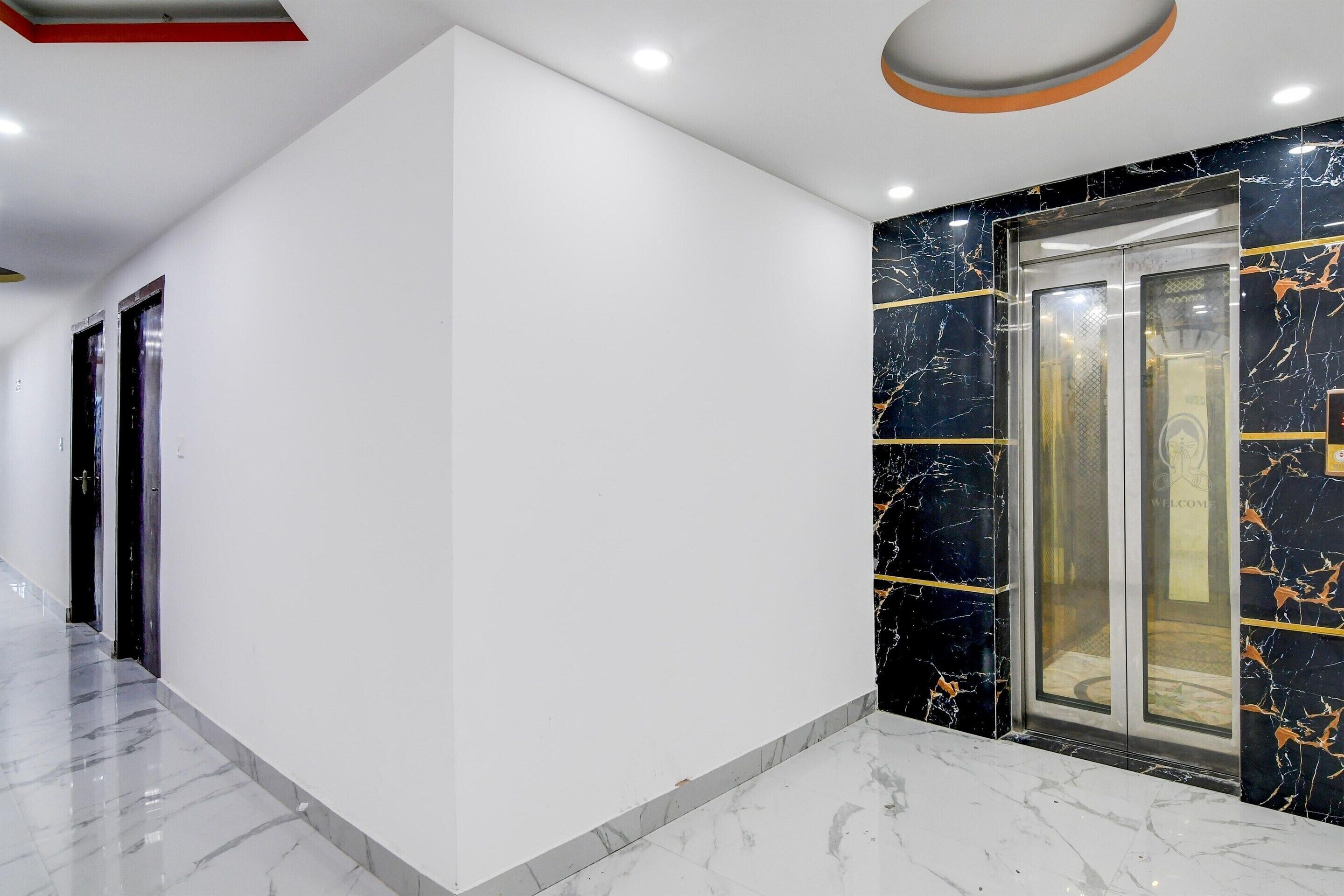 A modern hallway with a marble floor, a black marble wall with gold accents, and a glass elevator.