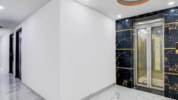 A modern hallway with a marble floor, a black marble wall with gold accents, and a glass elevator.