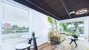 A modern living room with a sofa, a glass coffee table, and a dining area with a round table and stools. - Stay Park Cruise Modern Loft by Port -unit 200 (Cape Canaveral)