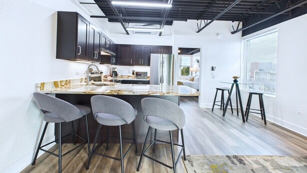 A modern kitchen with dark cabinets, a marble countertop, and a bar area with stools. - Stay Park Cruise Modern Loft by Port -unit 200 (Cape Canaveral)