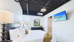 Une chambre d’hôtel moderne équipée d’un lit, d’un bureau, d’une lampe, d’un tableau et d’un téléviseur fixé au mur.