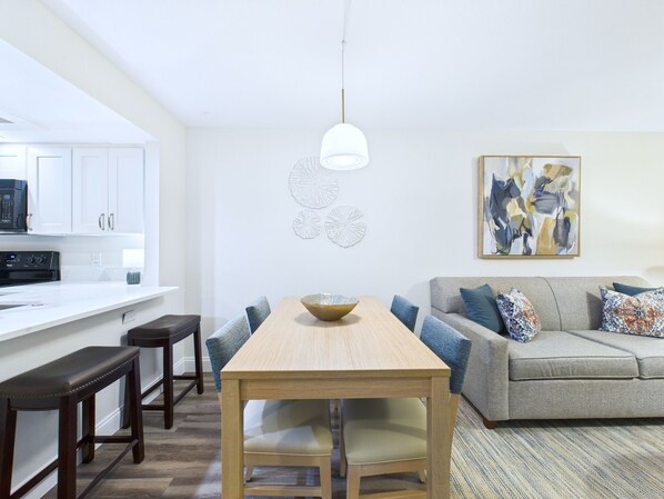 A modern kitchen with white cabinets, a black microwave, and a wooden dining table with chairs. - La Cita Country Club 2BR Condo (Titusville)