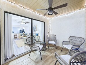 A room with wicker chairs, a ceiling fan, and a view of a kitchen and dining area through large windows. - La Cita Country Club 2BR Condo (Titusville)