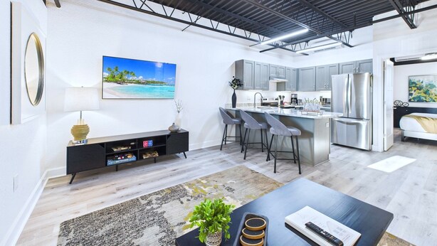 A modern kitchen with grey cabinets, stainless steel appliances, and a central island with bar stools. - Stylish Loft Minutes From Beach Port - Unit 204 (Cape Canaveral)