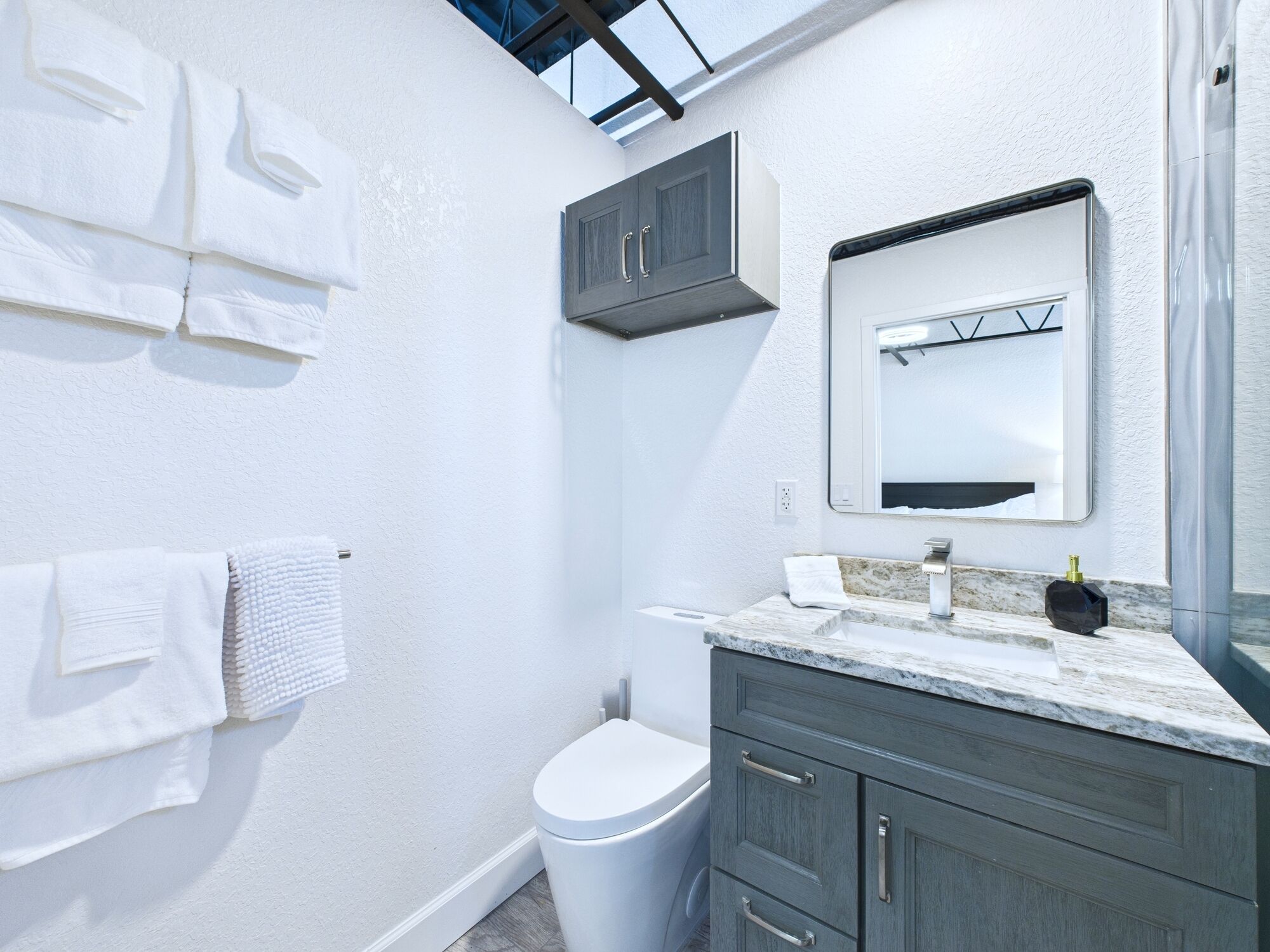 Une salle de bain moderne avec des murs blancs, un comptoir en marbre, des toilettes et un meuble.