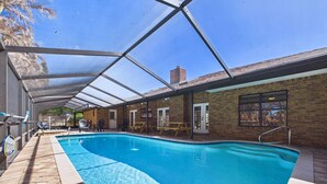 An indoor swimming pool with a clear roof, a brick building, and a wooden deck. - Indian Harbor Beach Pool Retreat (Indian Harbour Beach)