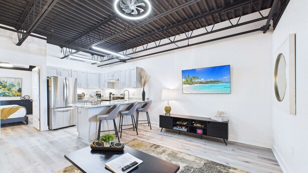 A modern kitchen with stainless steel appliances, a dining area with a black table and chairs, and a large window with a view of the ocean. - Sleek Coastal Loft Close to Port Beach -unit 205 (Cape Canaveral)