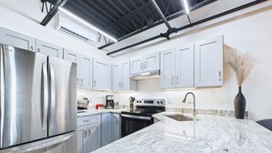 A modern kitchen with stainless steel appliances, white cabinets, and a marble countertop. - Sleek Coastal Loft Close to Port Beach -unit 205 (Cape Canaveral)