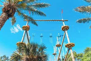Una estructura alta con varios niveles y cuerdas, rodeada de palmeras y un cielo azul claro.