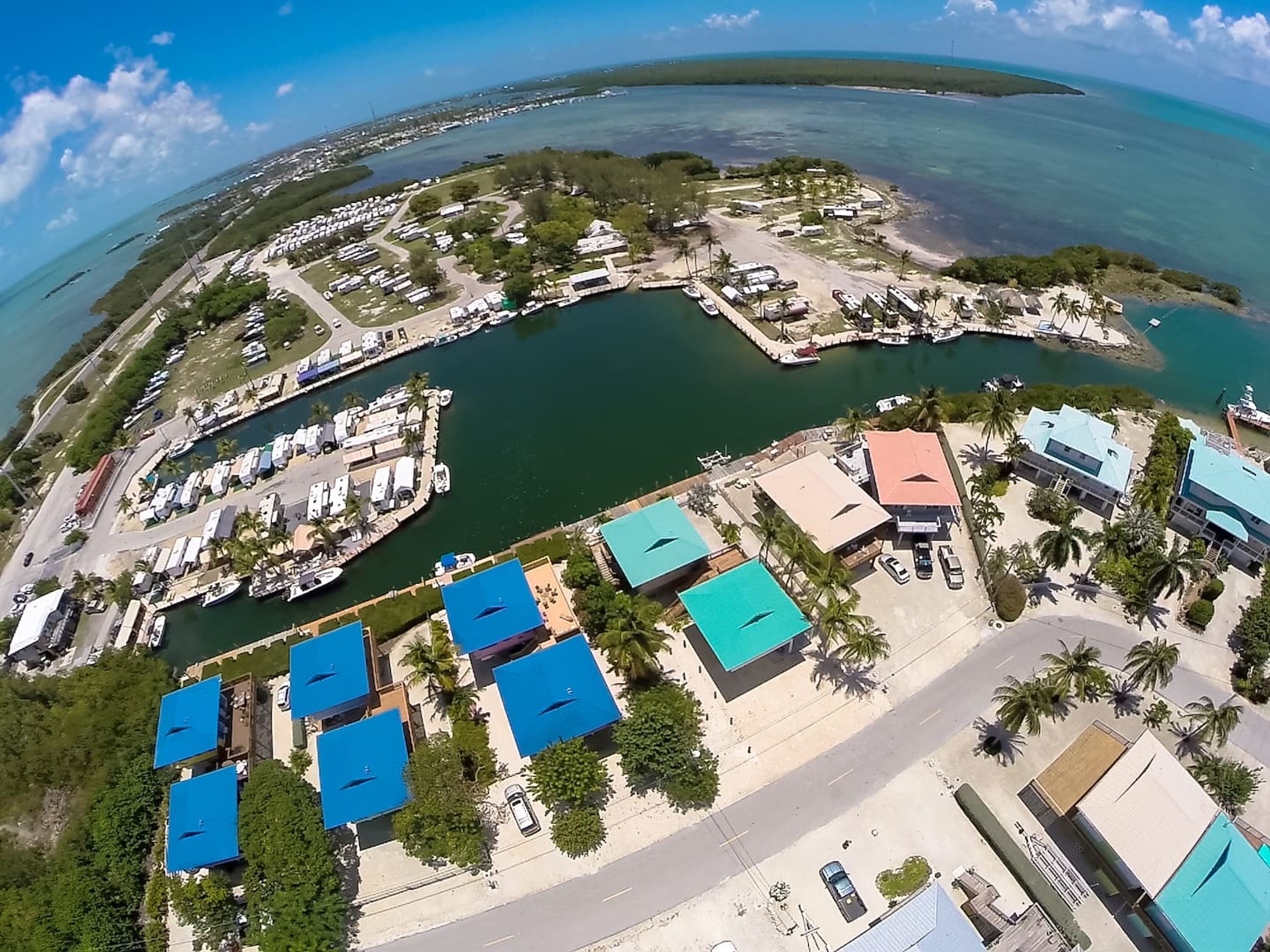 Vista aérea de una zona costera con vehículos recreativos, barcos y edificios con techos azules.