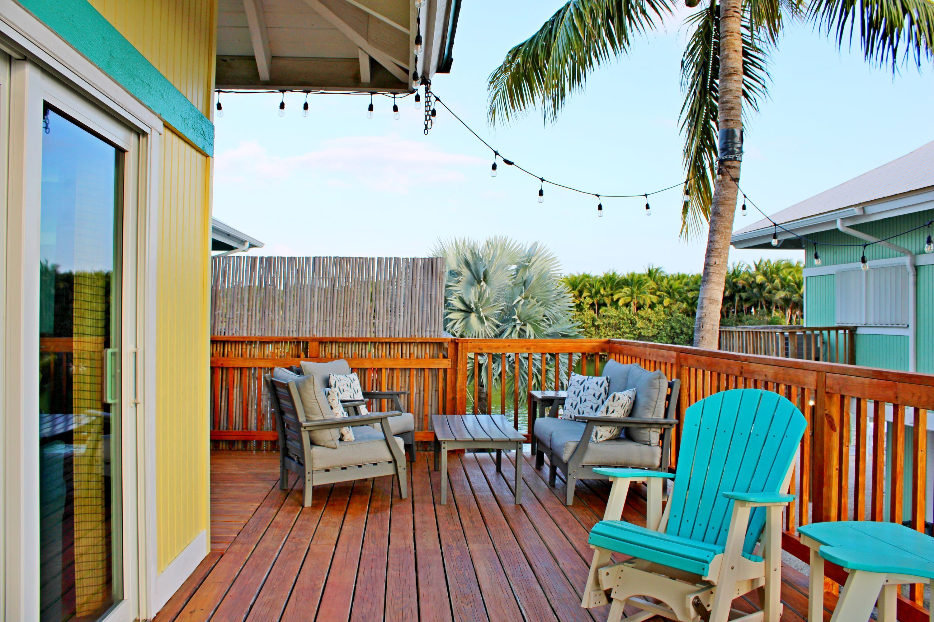 A wooden deck with outdoor furniture, a palm tree, and string lights.