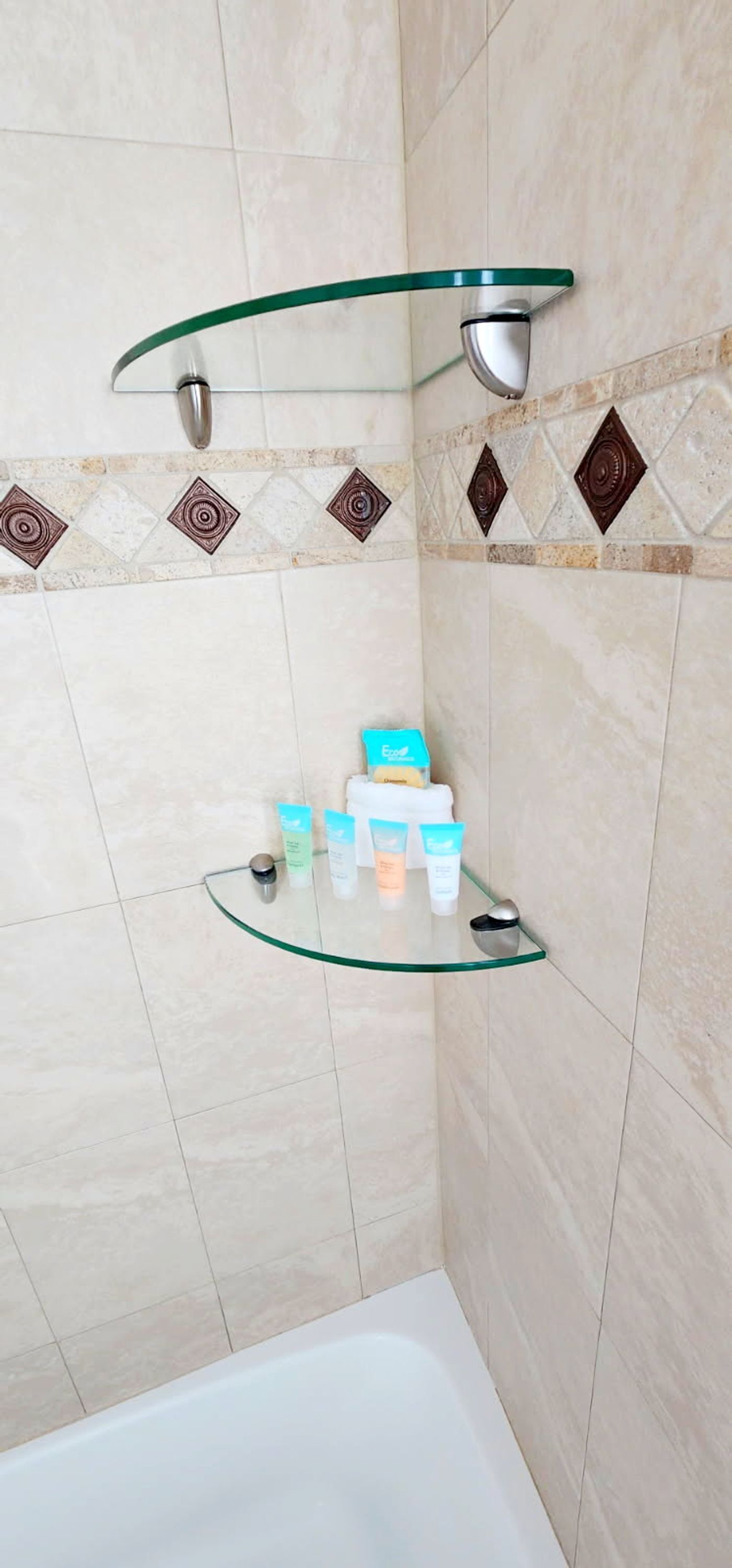 Une salle de bain avec une étagère en verre pour les articles de toilette, un siège de douche en verre et une baignoire.