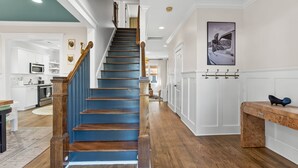 Eine Treppe mit Holzboden und einem blauen Geländer, die zu einem Raum mit weißen Wänden und einer Küche im Hintergrund führt.