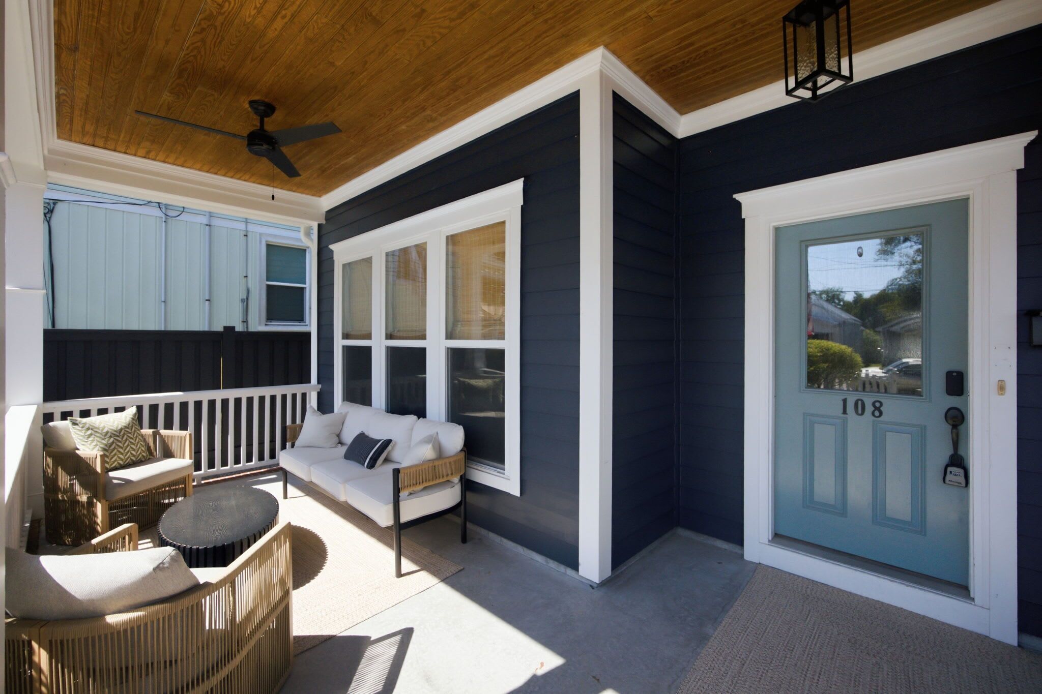 A covered porch with a seating area, a door with a number, and a ceiling fan.