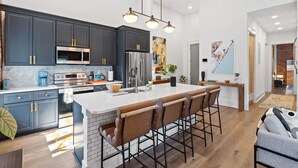 A modern kitchen with dark cabinets, a large island with bar stools, a microwave, stove, and refrigerator. - OneTreeHill Loft Downtown, Riverwalk, Live Oak (Wilmington)