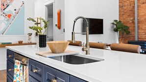 A modern kitchen with a white countertop, a double sink, and a wooden bowl centerpiece. - OneTreeHill Loft Downtown, Riverwalk, Live Oak (Wilmington)