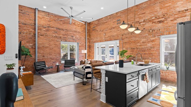 A spacious kitchen with a brick wall, a large island, and a dining area with a sofa and chairs. - OneTreeHill Loft Downtown, Riverwalk, Live Oak (Wilmington)