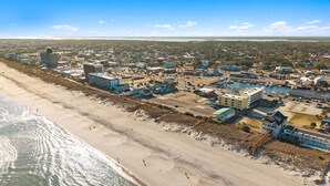 Vue aérienne d’une ville côtière avec une plage, des bâtiments et un port de plaisance.