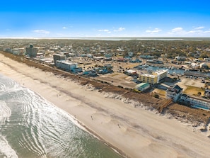 Vue aérienne d’une ville côtière avec une plage, des bâtiments et un port de plaisance.